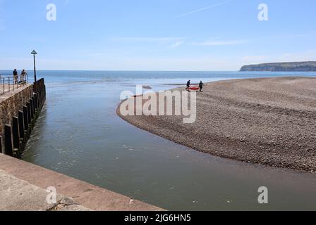 AXMOUTH, DEVON, ENGLAND - JULI 12. 2020: Zwei Menschen tragen ihre Kanus über den Schindelspieß, da sie den Strom in der Mündung des Th nicht schlagen können Stockfoto