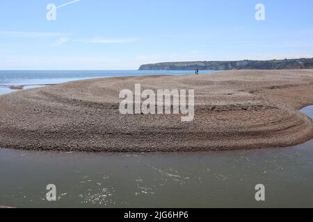 AXMOUTH, DEVON, ENGLAND - JULI 12. 2020: Ein Mann und eine Frau stehen auf der Schindelspieß in der Nähe von Axmouth und blicken auf das Meer Stockfoto