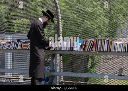 Ein chassidischer orthodoxer jüdischer Mann stösst bei einem Verkauf religiöser Bücher im Freien nach. An der Lee Avenue in Williamsburg, Brooklyn, New York City. Stockfoto