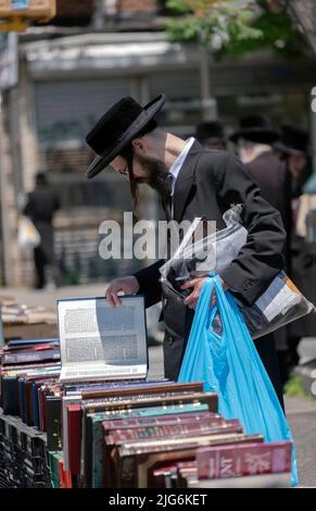 Ein chassidischer orthodoxer jüdischer Mann stösst bei einem Verkauf religiöser Bücher im Freien nach. An der Lee Avenue in Williamsburg, Brooklyn, New York City. Stockfoto