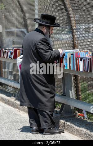 Ein chassidischer orthodoxer jüdischer Mann stösst bei einem Verkauf religiöser Bücher im Freien nach. An der Lee Avenue in Williamsburg, Brooklyn, New York City. Stockfoto