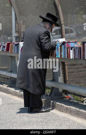 Ein chassidischer orthodoxer jüdischer Mann stösst bei einem Verkauf religiöser Bücher im Freien nach. An der Lee Avenue in Williamsburg, Brooklyn, New York City. Stockfoto