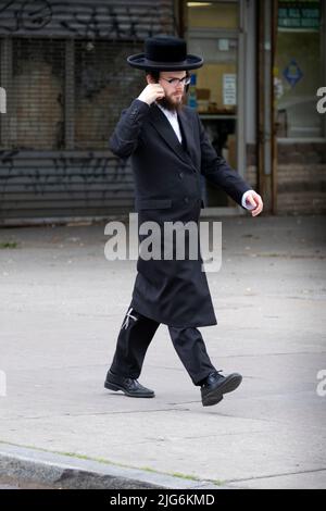 Ein orthodoxer jüdischer Mann mittleren Alters geht auf der Lee Avenue, während er seinen Peyot anpasst. In williamsburg, Brooklyn, New York City. Stockfoto