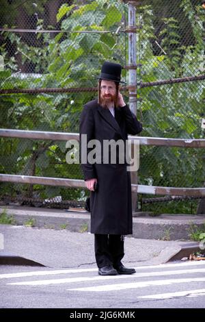 Ein orthodoxer jüdischer Mann mit langem roten Peyus wartet darauf, die Straße zu überqueren. In Williamsburg, Brooklyn, New York City. Stockfoto