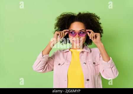 Portrait of adorable sorglos Mädchen Hände berühren Gläser schauen interessiert leeren Raum isolaetd auf grünem Hintergrund Stockfoto