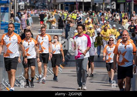 High Street, Southend on Sea, Essex, Großbritannien. 8. Juli 2022. Der Baton Relay der Queen hat die neue Stadt Southend on Sea auf seiner Reise nach Birmingham für die Commonwealth Games erreicht und wurde von ausgewählten Batonbearern von einem Ende der High Street zum anderen getragen. Sam Bennett, Jugendathlet mit Goldmedaille, nahm die erste Etappe an der Spitze der Prozession die High Street hinunter Stockfoto