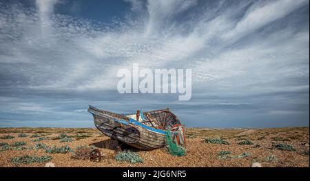 Am Kiesstrand von Dungeness Headland in Kent befinden sich mehrere alte, aboned Fischerboote Stockfoto