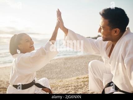 Abschluss einer weiteren erfolgreichen Sunset Session. Aufnahme von zwei jungen Kampfkünstlern, die sich beim Karate-Training am Strand gegenseitig eine hohe fünf geben. Stockfoto