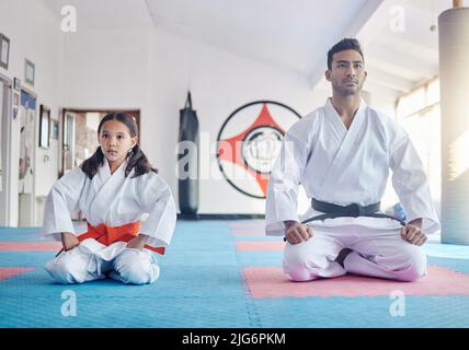 Im Ernst, bringen Sie Ihren Kindern Selbstverteidigung bei. Aufnahme eines jungen Mannes und eines niedlichen kleinen Mädchens, das in einem Studio Karate praktiziert. Stockfoto