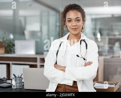 Qualifiziert und selbstbewusst. Ein beschnittenes Porträt einer attraktiven jungen Ärztin, die mit gefalteten Armen im Büro steht. Stockfoto