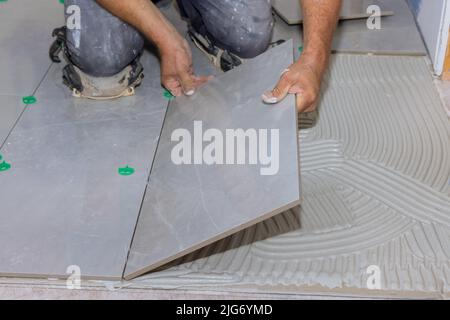 Mit Hilfe eines Hausbauarbeiters, indem Keramikfliesen auf einer Klebefläche Stockfoto