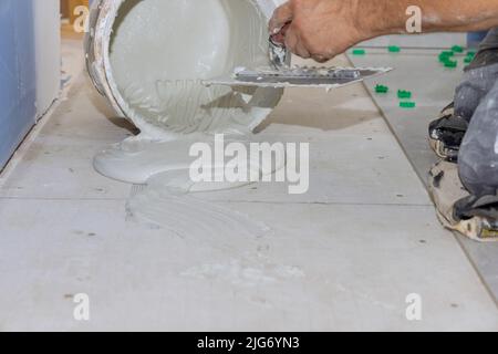 Als Vorbereitung für die Verlegung von Bodenfliesen trägt der Kelle Klebstoff auf einen Betonboden auf Stockfoto