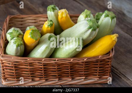 Mehrfarbige Zucchini-Gelb, Grün, Weiß, Orange auf dem Holztisch aus nächster Nähe. Hintergrund der Speisen. Frisch geernteter Zucchini im Korb, zugeschnittenes Sommerkürbis. Gepflückte grüne Zucchini. Stockfoto