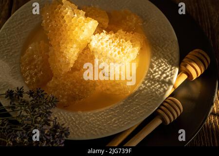 Honig und Waben auf einem weißen Teller. Süßes Essen in einer Schüssel auf dem Tisch. Ein Produkt der Imkerei. Lavendelblüte. Stockfoto