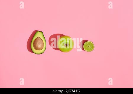 Lebensmitteldesign. Zusammensetzung aus frischen Früchten, Avocado grünen Apfel und die Hälfte der geschnittenen Avocado auf rosa Korallen Hintergrund Stockfoto