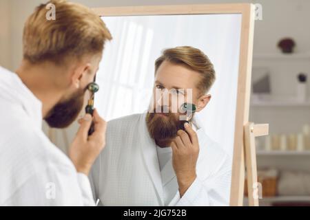 Kaukasischen Mann verwenden Roller Massage Gesicht tun Schönheitsverfahren Stockfoto