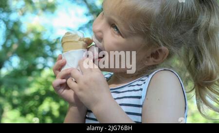 Nettes kleines Mädchen isst draußen Eis. Nahaufnahme eines blonden Mädchens, das auf der Parkbank sitzt und Eis isst. Odessa Ukraine Stockfoto