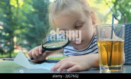 Kleines Mädchen schaut vorsichtig in die Linse auf das Salz. Nahaufnahme des blonden Mädchens studiert Salzkristalle, während sie durch Vergrößerungen betrachtet wird Stockfoto