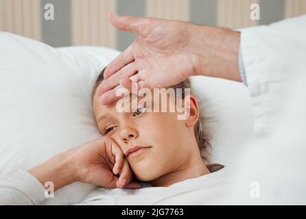 Achten Sie auf Ihren Körper. Aufnahme eines nicht erkennbaren Arztes, der die Temperatur eines kranken kleinen Mädchens zu Hause überprüft. Stockfoto