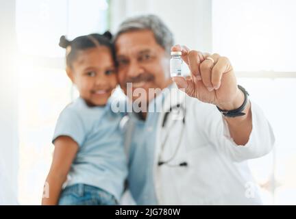 Es wird Sie vor zukünftigen Krankheiten schützen. Aufnahme eines reifen Arztes, der während einer Untersuchung mit einem kleinen Mädchen zu Hause ein Impffläschchen in der Hand hält. Stockfoto