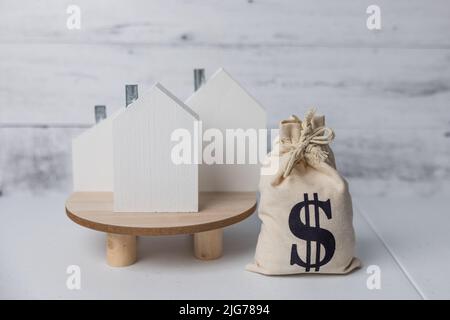 Ein Geldbeutel und Holzhäuser symbolisieren die steigenden Kosten für Wohnungen und den Immobilienmarkt aufgrund der Inflation in der Wirtschaft. Stockfoto