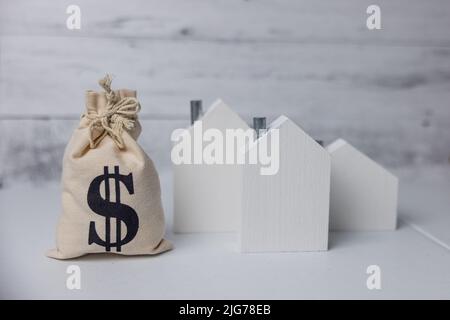 Ein Geldbeutel und Holzhäuser symbolisieren die steigenden Kosten für Wohnungen und den Immobilienmarkt aufgrund der Inflation in der Wirtschaft. Stockfoto