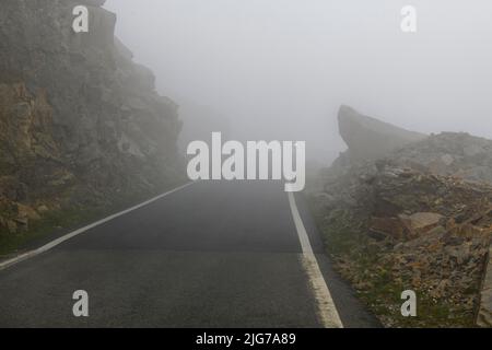 Niedrige Wolken auf kurvigen Bergstraße Pass am Gipfel des Colle del Nivolet, im Hintergrund Licht von entgegenkommenden Fahrzeug, Col du Nivolet, Graian Alps Stockfoto