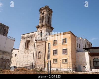 Eine verlassene Kirche mit einer verzierten, aber verdunkelten Fassade, die in der Abenddämmerung von Straßenlaternen in den Hinterstraßen von Nardo, Apulien, reflektiert wird. Stockfoto