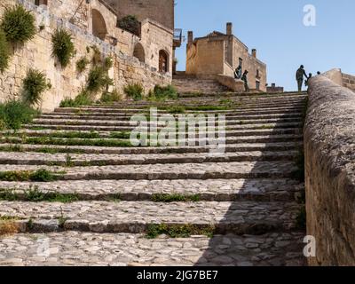 Stufen, die in der Altstadt oder in Sassi von Miera, Italien, bergauf führen, mit der Silhouette von Skulpturen menschlicher Formen an der Spitze der Treppe Stockfoto