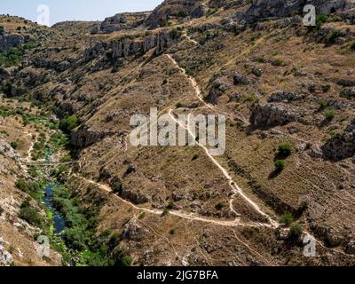 Abgenutzte Wanderwege durch die zerklüftete Landschaft des Tals La Gravina gegenüber dem Sassi von Miera, Italien mit seinen Höhlenwohnungen Stockfoto