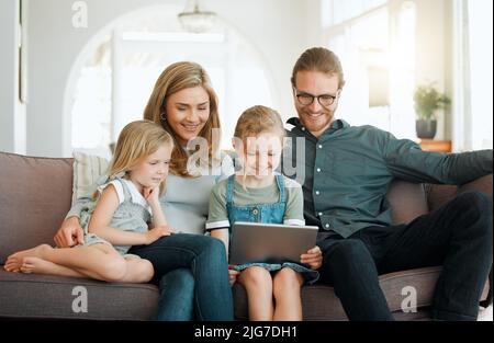 Kinder nehmen heutzutage so schnell Dinge auf. Aufnahme einer jungen Familie, die zusammen auf dem Sofa sitzt und sich mit einem digitalen Tablet verbindet. Stockfoto