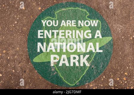 Sie betreten nun Ein Nationalparkschild, das grün auf den Zement gemalt wurde. Stockfoto