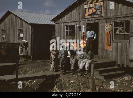 Wanderarbeiter außerhalb eines „Juke Joint“ während einer lockeren Saison, Belle Glade, Florida. [Schilder, die für Jax eiskaltes Bier, Royal Crown Cola und Coca-Cola werben]. Stockfoto