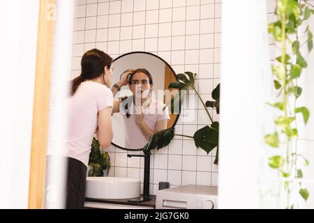 Bild einer kaukasischen nicht-binären Trans-Frau, die im Badezimmer den Spiegel ansah Stockfoto