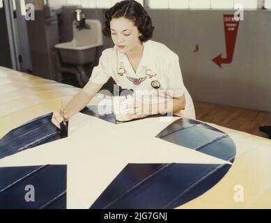 Die amerikanischen Insignien auf Flugzeugflügeln zu malen, ist eine Aufgabe, die Frau Irma Lee McElroy, eine ehemalige Büroangestellte, mit Präzision und patriotischem Eifer macht. Frau McElroy ist Angestellte des öffentlichen Dienstes am Marineflugplatz, Corpus Christi, Texas. Ihr Mann ist Fluglehrer. Stockfoto