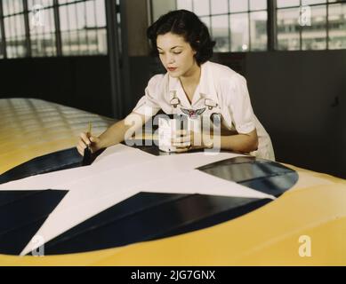 Die amerikanischen Insignien auf Flugzeugflügeln zu malen, ist eine Aufgabe, die Frau Irma Lee McElroy, eine ehemalige Büroangestellte, mit Präzision und patriotischem Eifer macht. Frau McElroy ist Angestellte des öffentlichen Dienstes am Naval Air Base, Corpus Christi, Texas. Ihr Mann ist Fluglehrer. Stockfoto