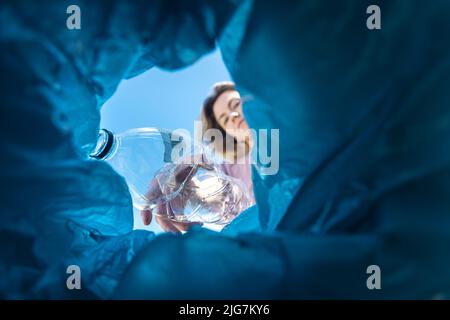 Eine Frau wirft eine Plastikflasche in den Müll. Nahaufnahme aus dem Mülleimer Stockfoto