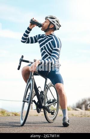 Ausreichend hydratisiert bleiben. In voller Länge ein hübscher, reifer Mann, der beim Radfahren im Freien eine Wasserpause einnimmt. Stockfoto