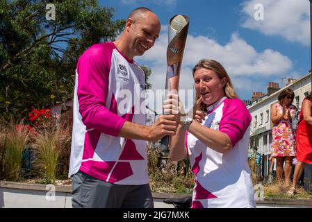High Street, Southend on Sea, Essex, Großbritannien. 8. Juli 2022. Der Baton Relay der Queen hat die neue Stadt Southend on Sea auf seiner Reise nach Birmingham für die Commonwealth Games erreicht und wurde von ausgewählten Batonbearern von einem Ende der High Street zum anderen getragen. Die zweite Person, die den Staffelstab auf diesem Bein trug, war Lisa Whymark (eine Gewinnerin des Points of Light Awards für Gemeinschaftsarbeit), die hier an den Olympiateilnehmer Dean Macey überreichte Stockfoto