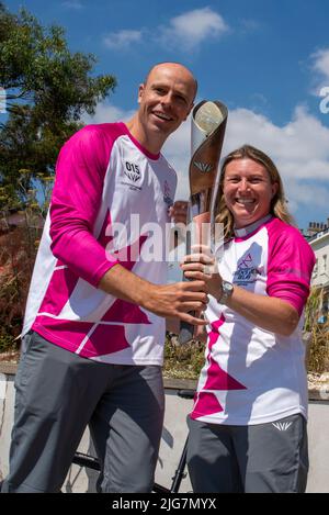 High Street, Southend on Sea, Essex, Großbritannien. 8. Juli 2022. Der Baton Relay der Queen hat die neue Stadt Southend on Sea auf seiner Reise nach Birmingham für die Commonwealth Games erreicht und wurde von ausgewählten Batonbearern von einem Ende der High Street zum anderen getragen. Die zweite Person, die den Staffelstab auf diesem Bein trug, war Lisa Whymark (eine Gewinnerin des Points of Light Awards für Gemeinschaftsarbeit), die hier an den Olympiateilnehmer Dean Macey überreichte Stockfoto