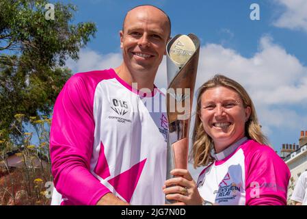 High Street, Southend on Sea, Essex, Großbritannien. 8. Juli 2022. Der Baton Relay der Queen hat die neue Stadt Southend on Sea auf seiner Reise nach Birmingham für die Commonwealth Games erreicht und wurde von ausgewählten Batonbearern von einem Ende der High Street zum anderen getragen. Die zweite Person, die den Staffelstab auf diesem Bein trug, war Lisa Whymark (eine Gewinnerin des Points of Light Awards für Gemeinschaftsarbeit), die hier an den Olympiateilnehmer Dean Macey überreichte Stockfoto