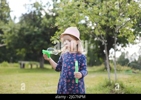 Nettes kleines Mädchen bläst Seifenblasen auf einem Spaziergang im Sommer im Freien Stockfoto