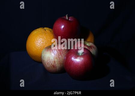 Rote Äpfel und Orangen auf schwarzem Hintergrund Stockfoto