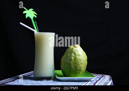 Grüne Guava-Frucht und ein Glas Guava-Saft auf schwarzem Hintergrund. Ideen für gesunde Bio-Getränke Stockfoto