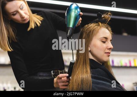 Friseurmeisterin trocknet die Haare des Mädchens mit einem Haartrockner und Kämmen nach dem Waschen im Schönheitssalon. Stockfoto
