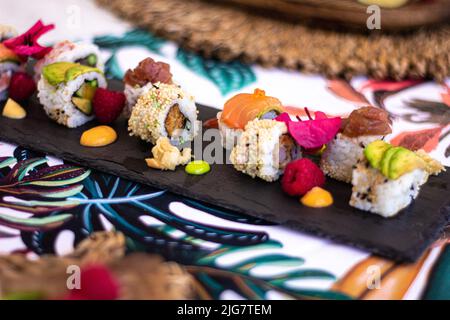 Eine selektive Nahaufnahme eines Sushi-Sets, garniert mit Früchten und Blumen vor einem verschwommenen Hintergrund Stockfoto