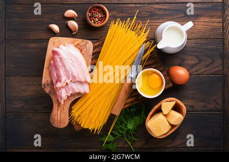 Zutaten für Pasta Carbonara. Traditionelle italienische Pasta Carbonara Zutaten Speck, Spaghetti, Parmesan und Eigelb, Knoblauch. Alter Tisch aus dunklem Holz Stockfoto