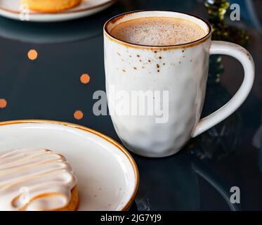Tasse mit Cappuccino oder Latte Kaffee und veganen Dessertkuchen auf blauem Glastisch Hintergrund und Bokeh Lichter im Café gesund essen vegetarische Lebensmittel Deli Stockfoto