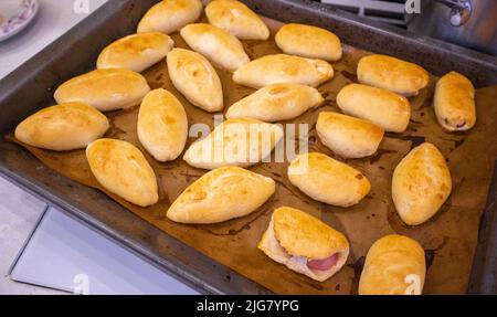 Legen Sie die frisch gebackenen Pasteten mit der Füllung auf ein mit Backpapier bedecktes Backblech. Köstliche frische hausgemachte Backwaren aus dem Ofen. Draufsicht. Stockfoto