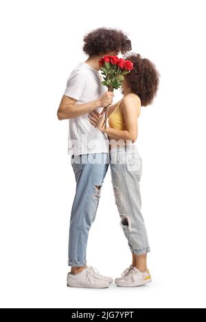 In voller Länge Profilaufnahme eines lässigen jungen Paares, das sich umarmt und ein paar rote Rosen auf weißem Hintergrund isoliert hält Stockfoto